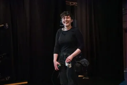 A stage management student smiling onstage while working on a production.