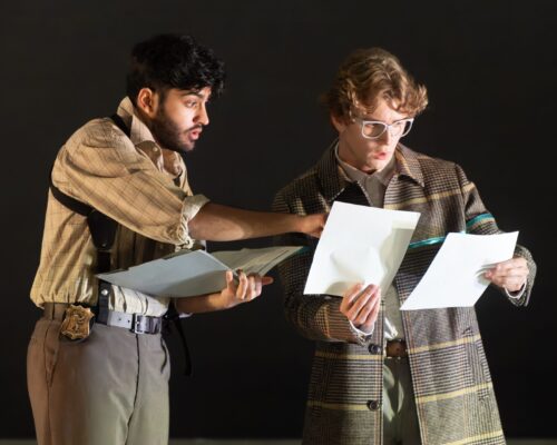 Two actors on stage looking at documents with confused and surprised expressions during a production of The City and The City