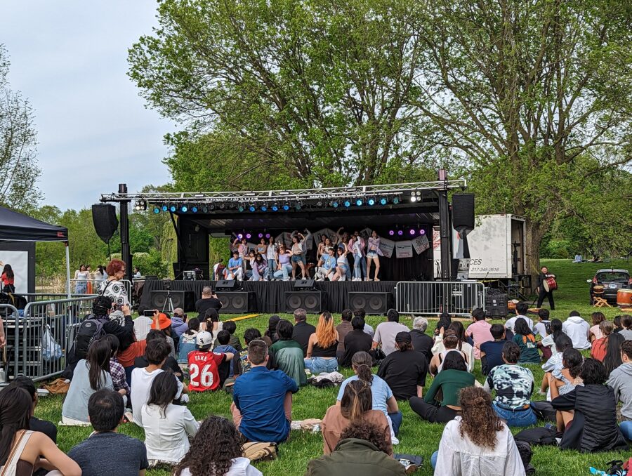 many people sitting on ground in front of stage with performers
