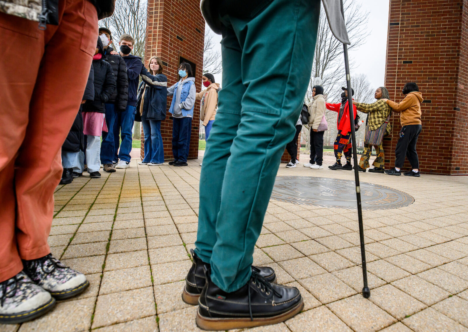 point of view from ground of line of people with person holding walking stick in the foreground