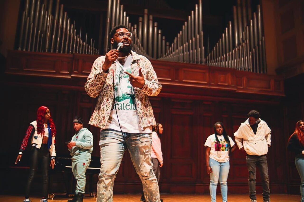 professor holden performs with a mic and several students at Smith Music Hall