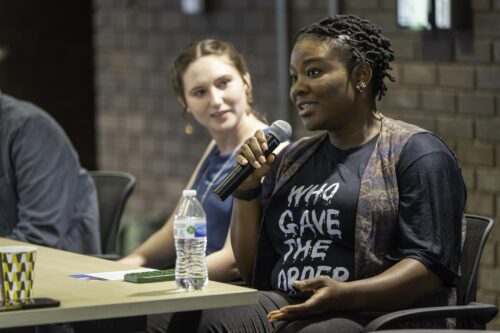 2 people at table, one speaks on handheld microphone