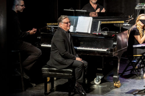 person sits at piano and smiles out to audience