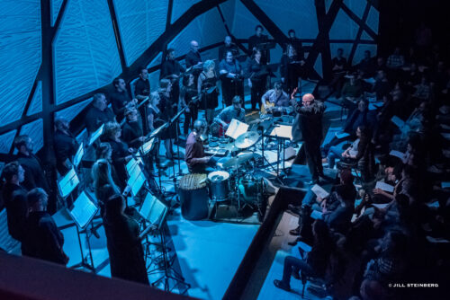 a chorus onstage with live musicians gathered around