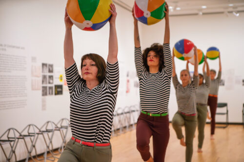several people wearing striped shirts hold up colorful beach balls 
